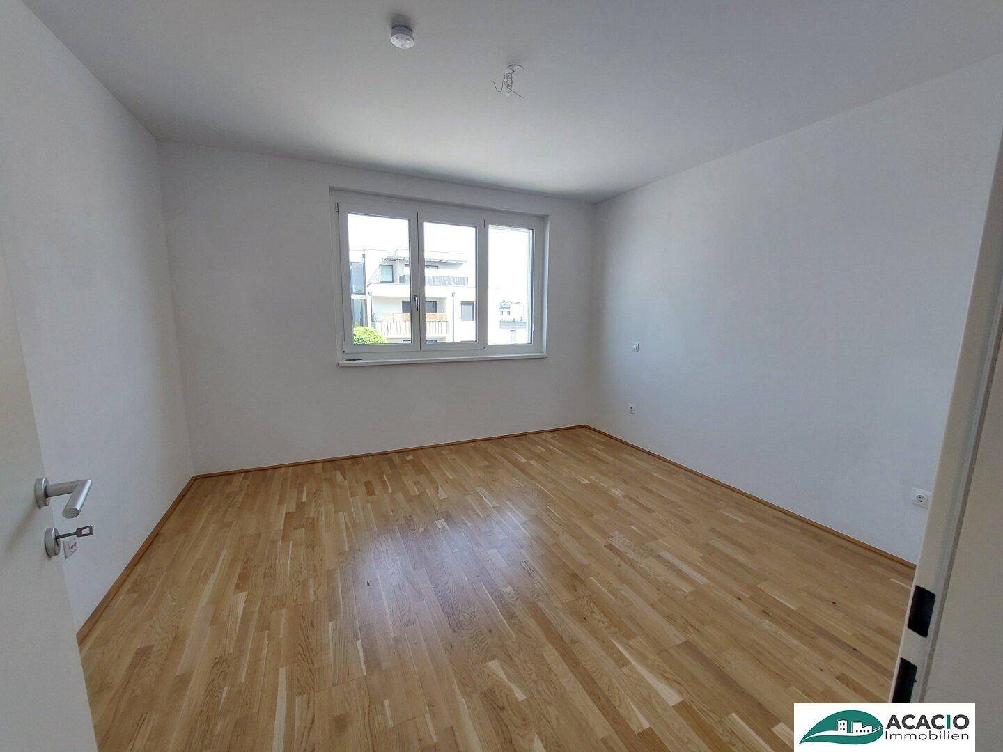 Helles Schlafzimmer mit Parkettboden und großem Fenster, bereit zum Einrichten.
