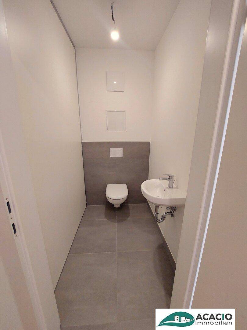 Modernes Gäste-WC mit Wand-WC, Waschbecken und grauen Fliesen.