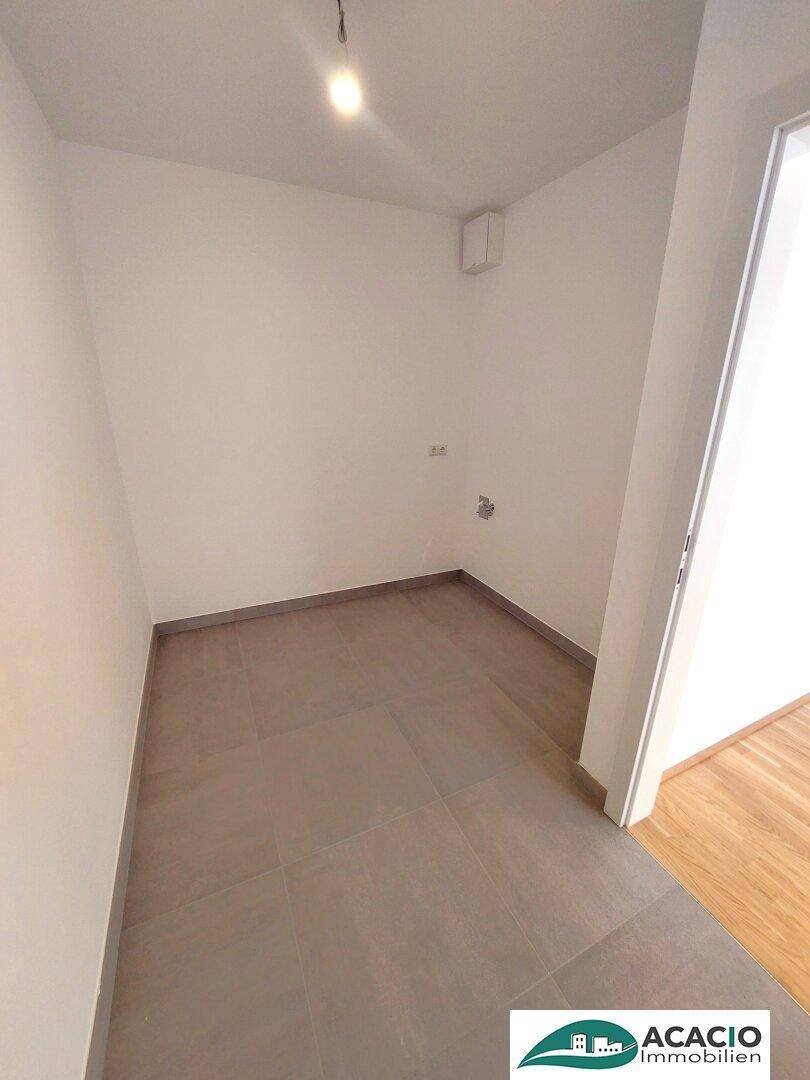 Praktischer Abstellraum mit grauen Fliesen und Anschlüssen für Haushaltsgeräte.