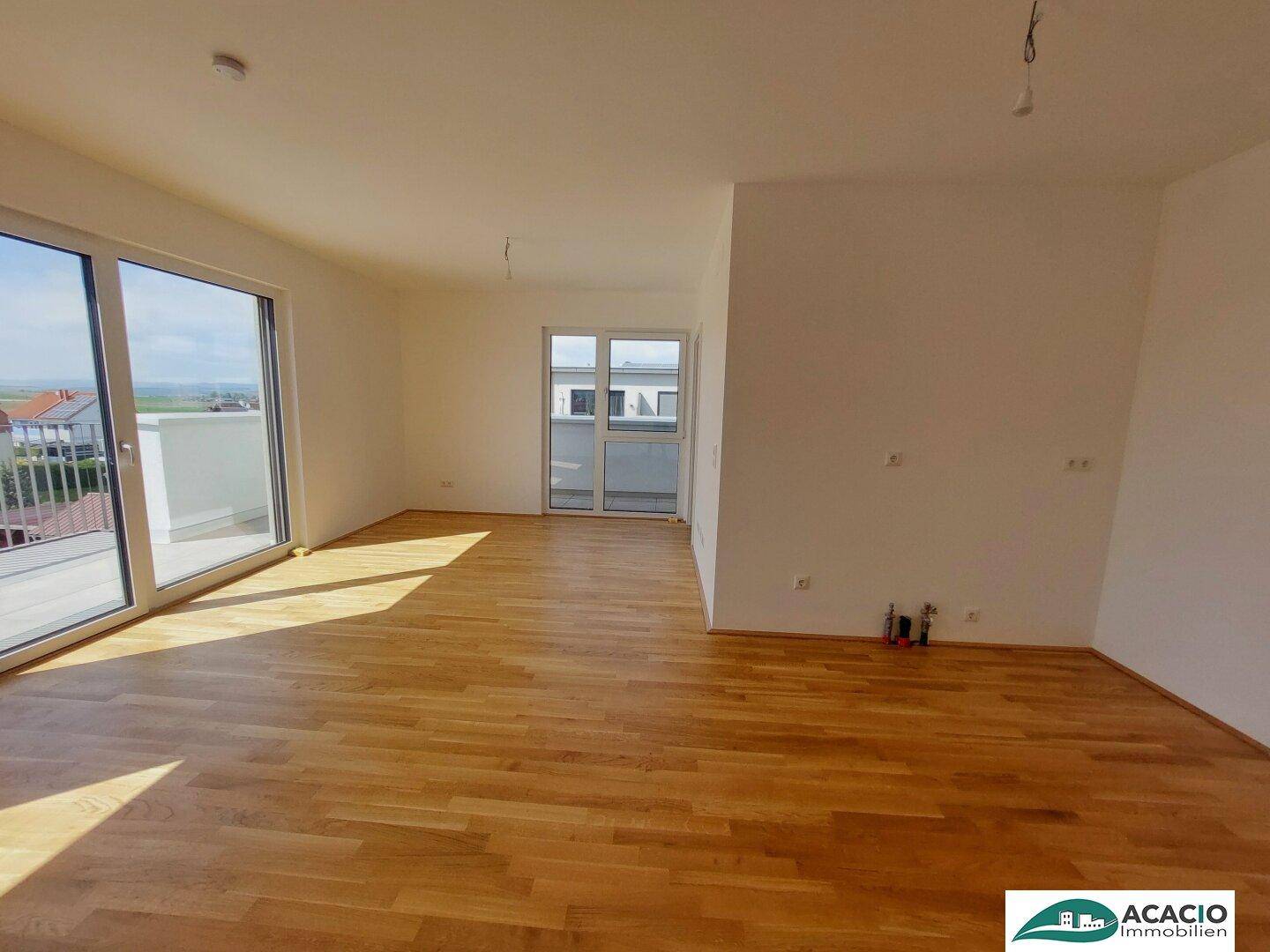 Geräumiges Wohnzimmer mit Holzboden und großen Fenstern, die viel Licht hereinlassen.