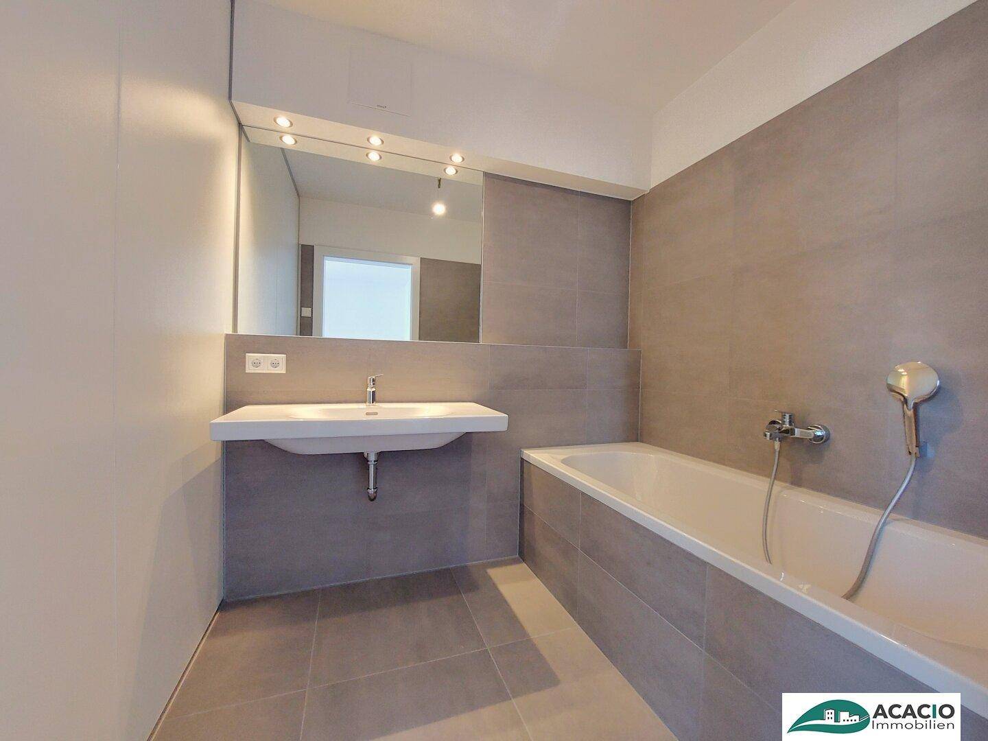 Modernes Badezimmer mit grauen Fliesen, Badewanne und einem einzelnen Waschbecken.