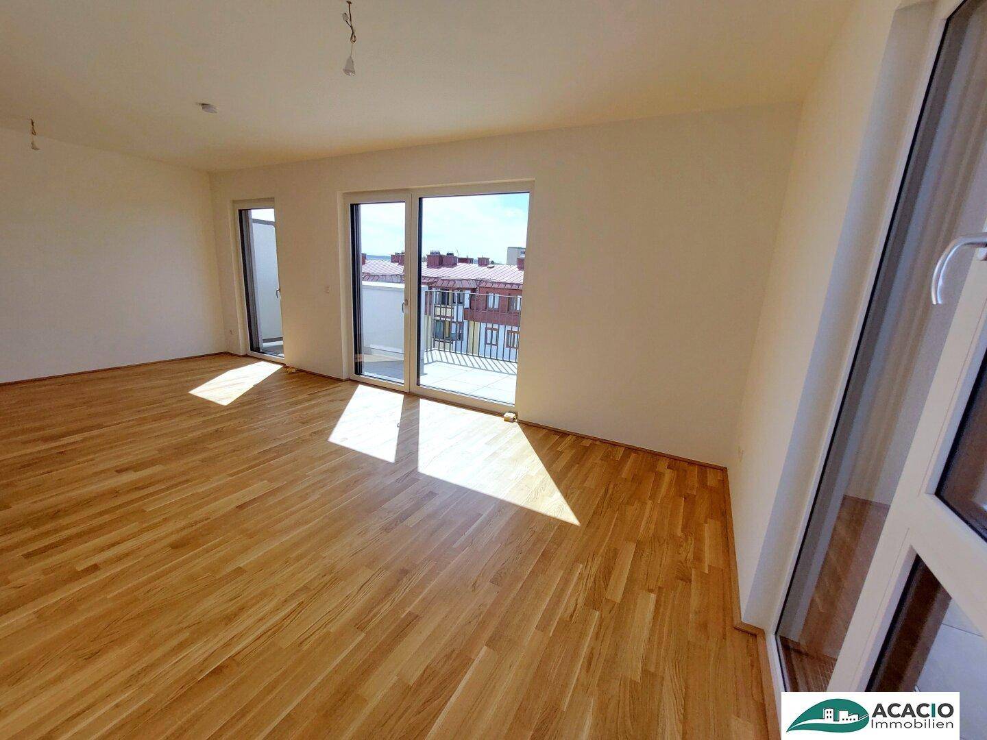Sonniges Wohnzimmer mit Parkettboden und großen Fenstern, die auf den Balkon führen.