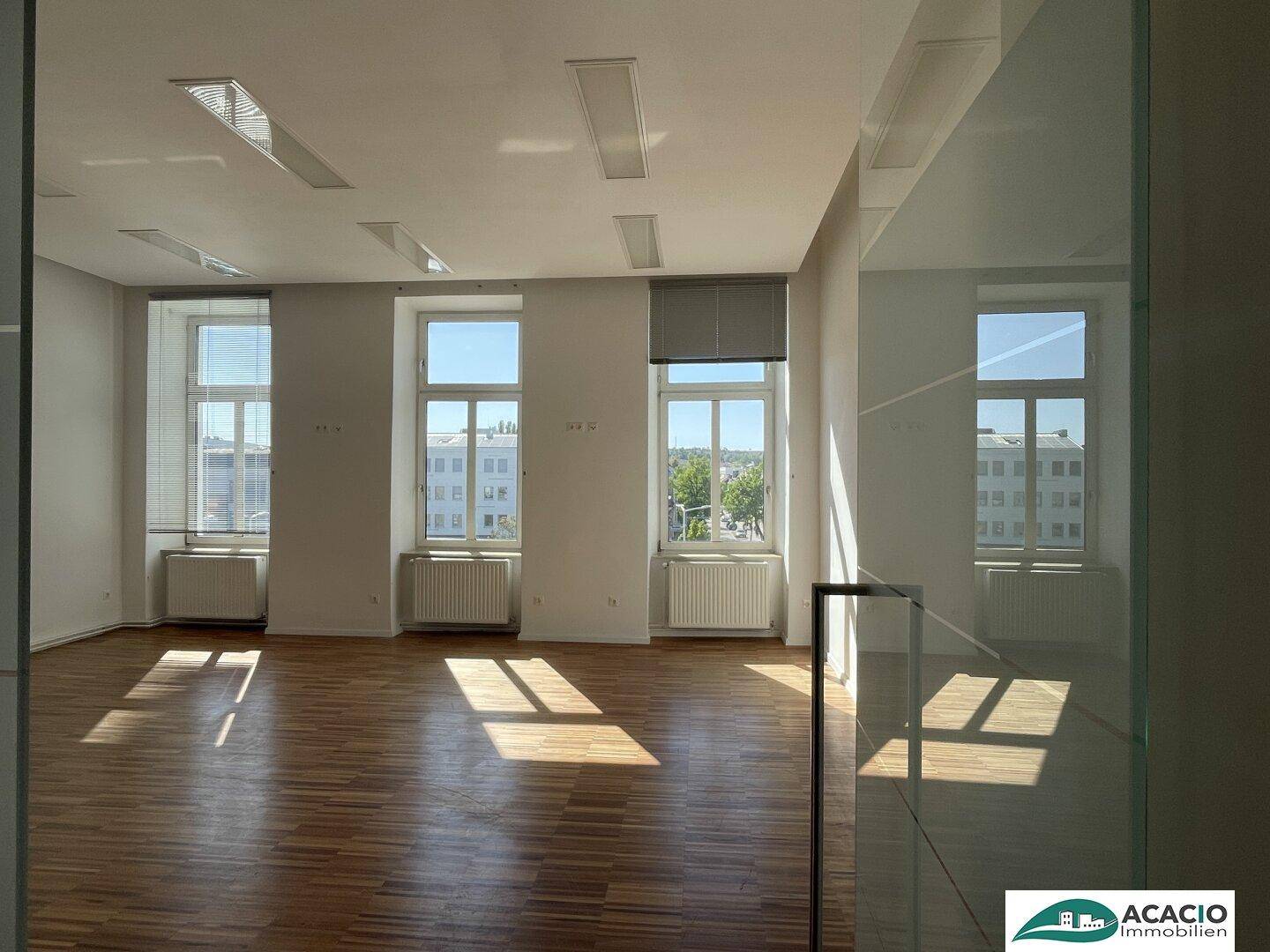 Heller Büroraum mit Holzboden und großen Fenstern, die viel Sonnenlicht hereinlassen.