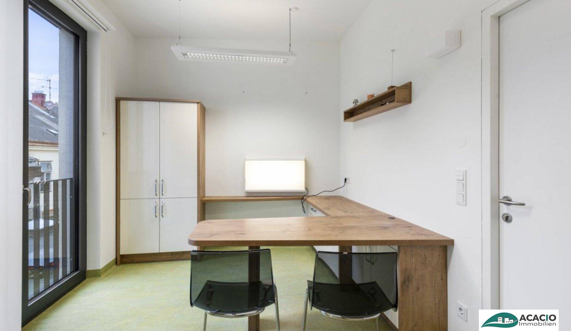 Helles Büro mit einem L-förmigen Holzschreibtisch, zwei Stühlen und einem Schrank, mit Balkonzugang.