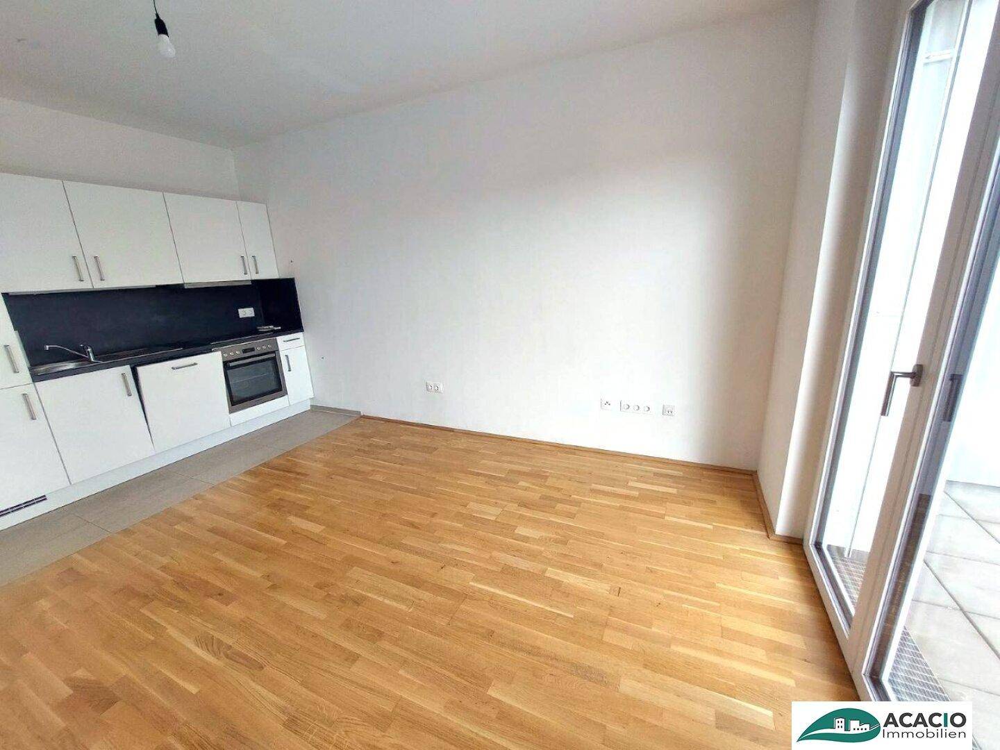 Offener Wohnbereich mit Küchenzeile, Parkettboden und Zugang zur Terrasse.