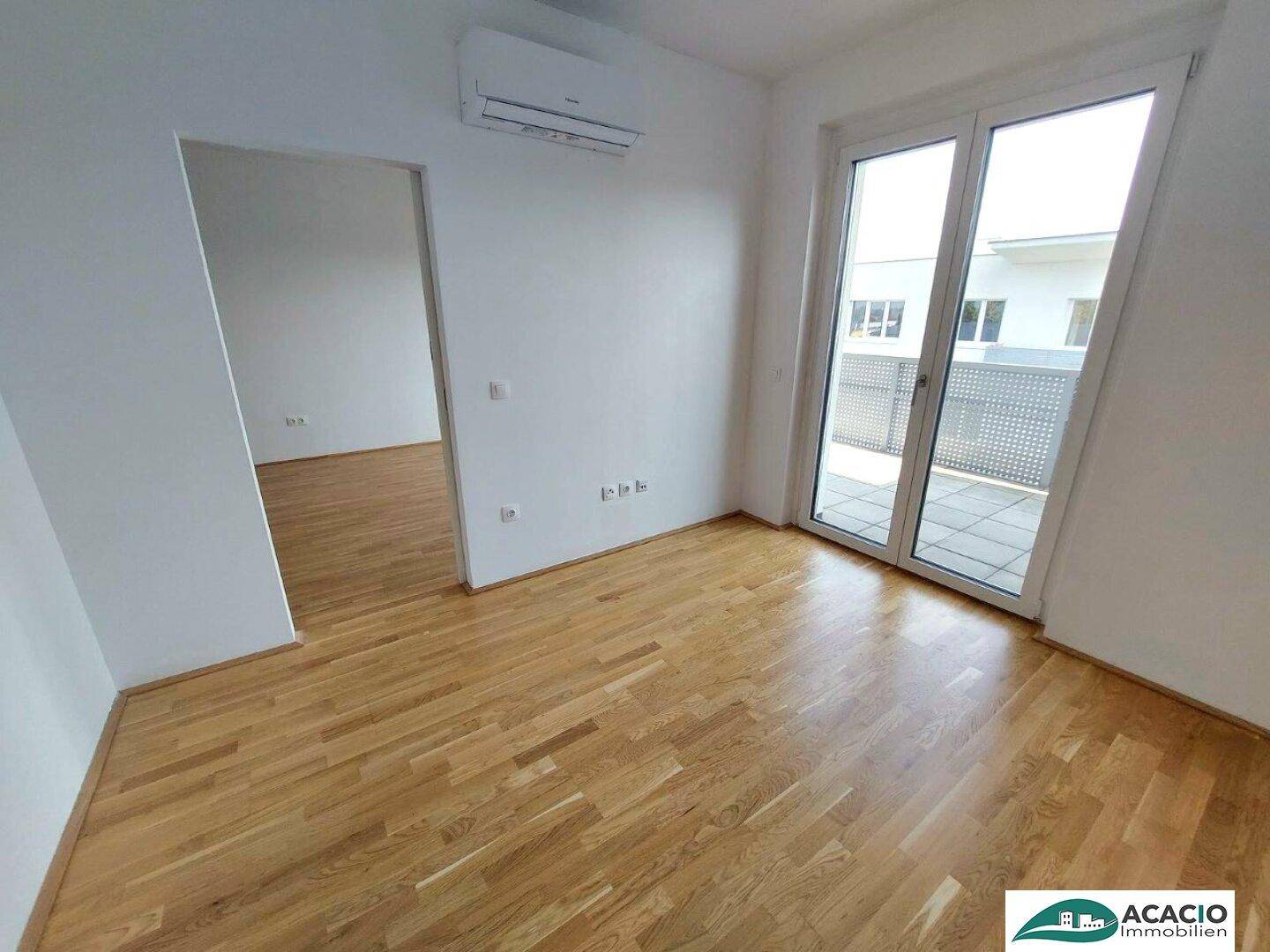 Helles Zimmer mit Parkettboden, Klimaanlage und Zugang zu einem Außenbereich.