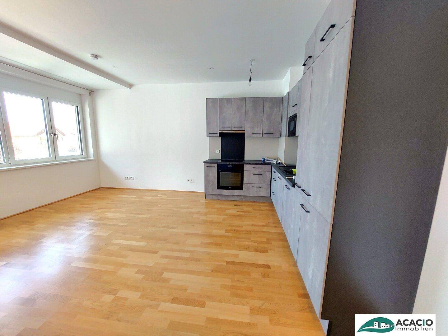 Moderne Küche mit grauen Schränken, integrierten Geräten und einem Fenster für Tageslicht.
