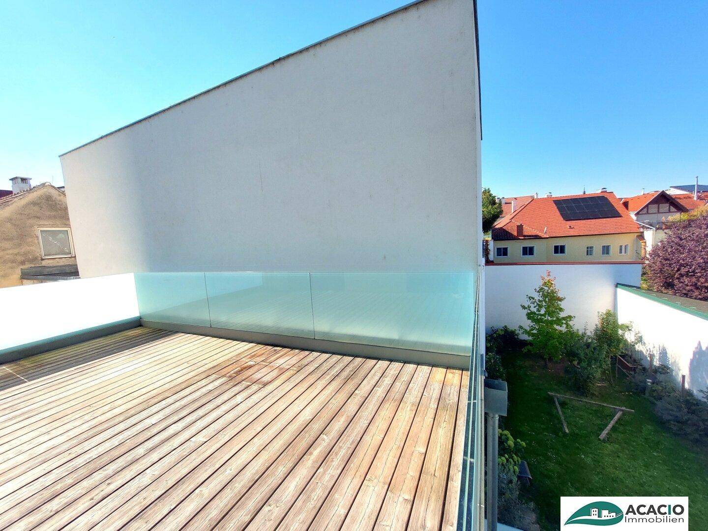 Große Holzterrasse mit Glasgeländer und Blick auf die umliegenden Häuser und Gärten.