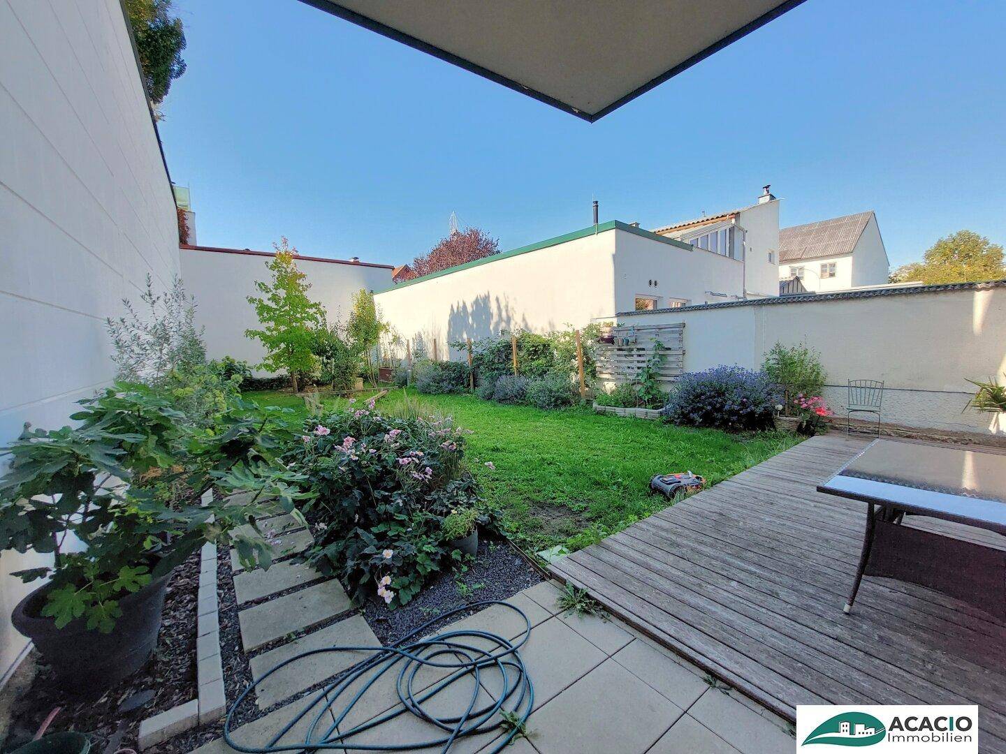 Gepflegter Gartenbereich mit Holzterrasse, Rasenfläche und verschiedenen Pflanzen im Freien.