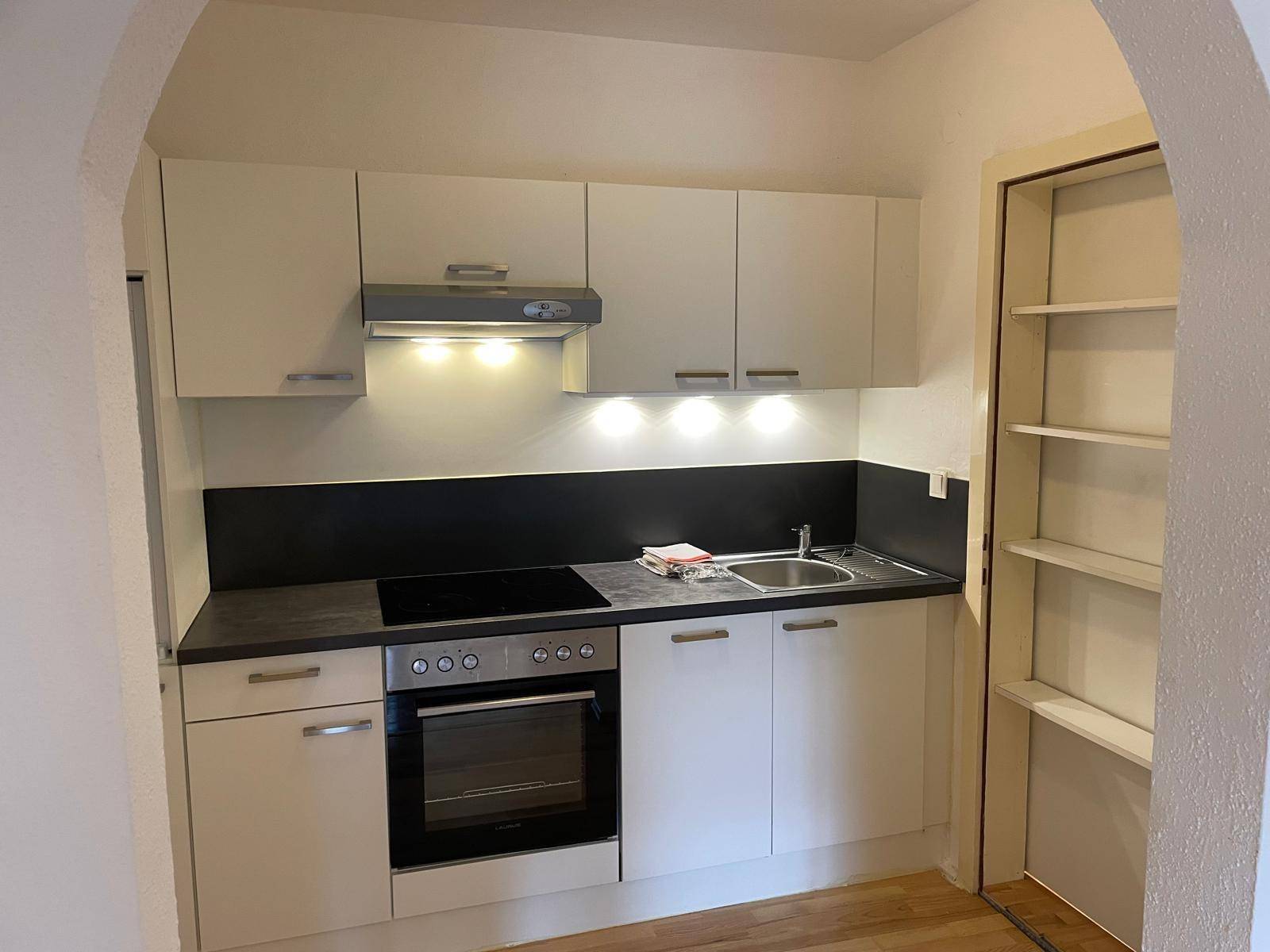Kompakte Einbauküche mit weißen Schränken, Induktionskochfeld und integriertem Backofen.