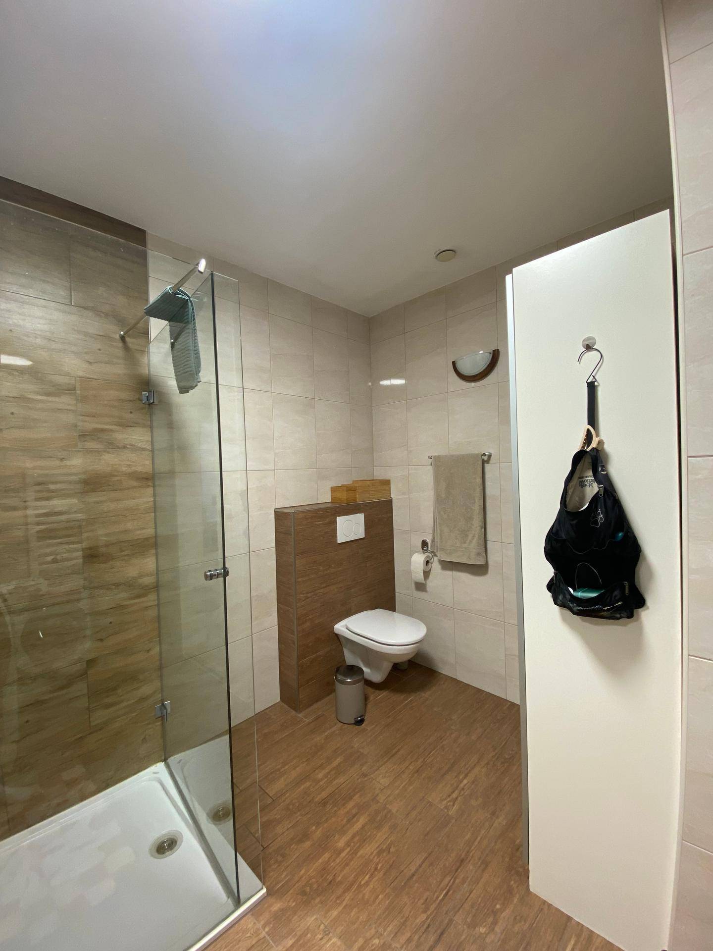 Modernes Badezimmer mit beigefarbenen Fliesen, einer begehbaren Dusche und Wand-WC.