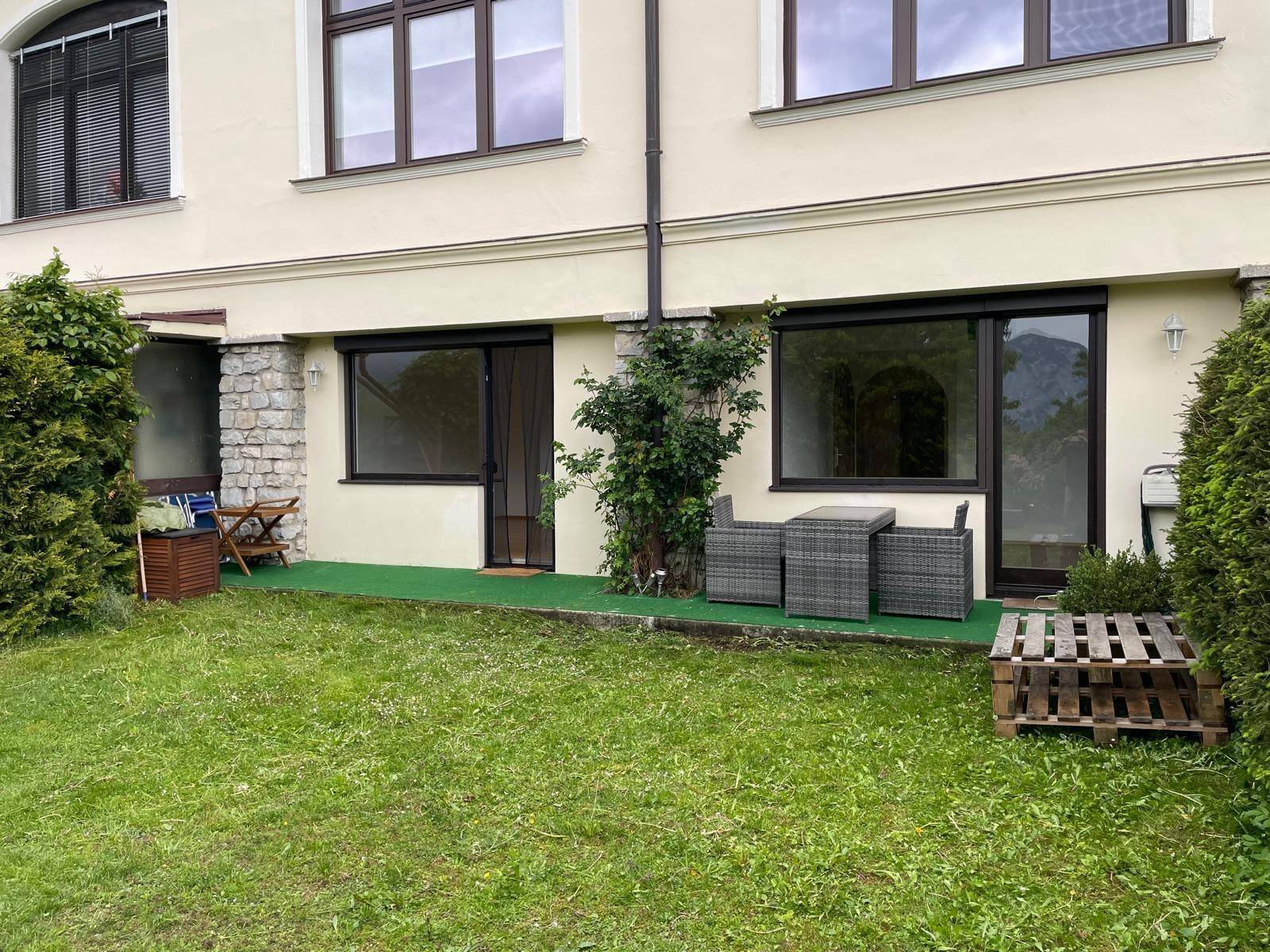 Gepflegter Gartenbereich mit Rasenfläche und einer kleinen möblierten Terrasse am Gebäude.