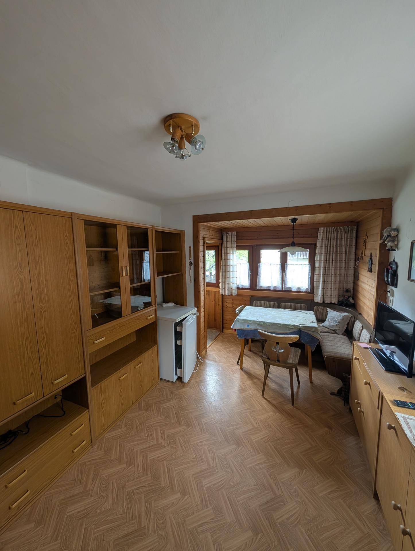 Wohn-Essbereich mit Holzmöbeln, kleinem Kühlschrank und Zugang zu einem Balkon.