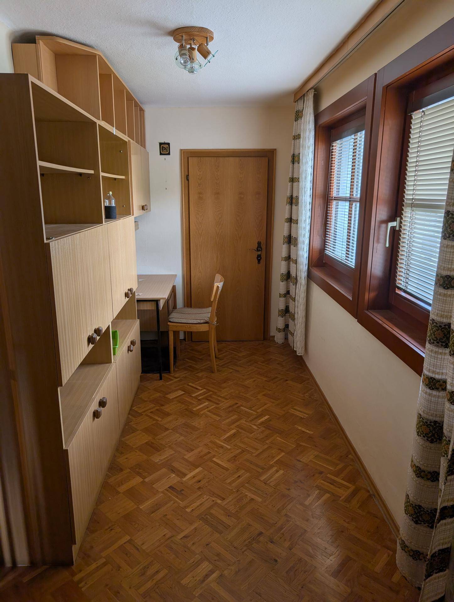 Kleiner Arbeitsbereich mit Holzregalen, Schreibtisch und Fenster mit Jalousien.