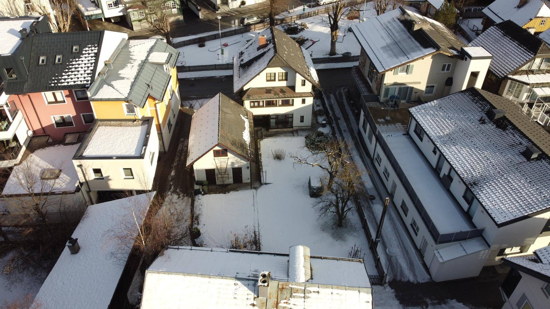 Vogelperspektive einer verschneiten Wohngegend mit Gärten und umliegenden Gebäuden.