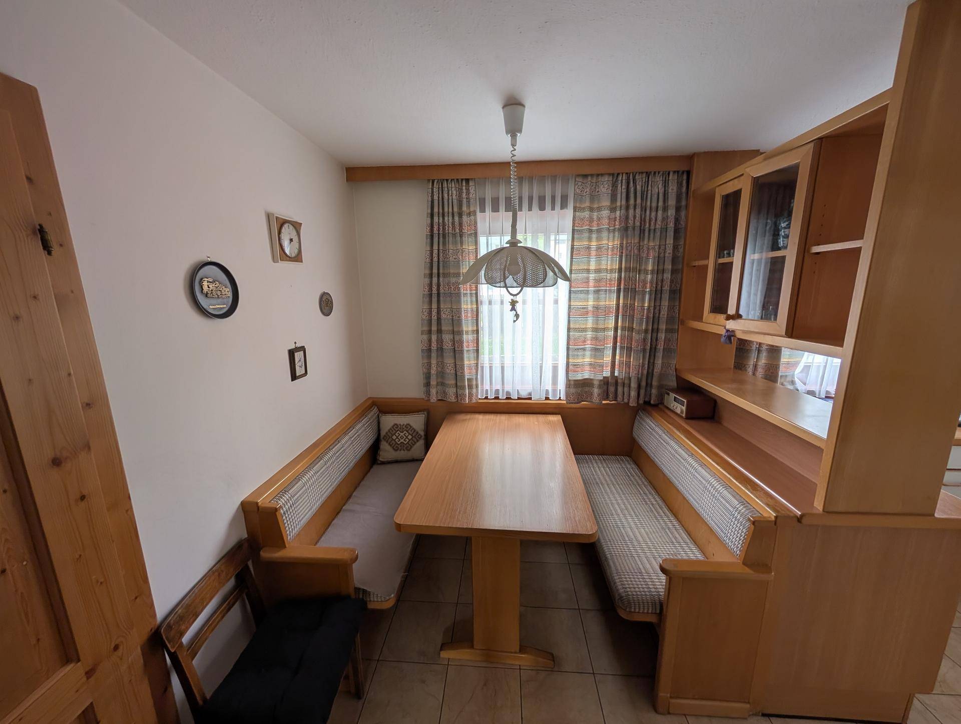 Helle Essecke mit Holzbänken, Esstisch und Fenster mit karierten Vorhängen.