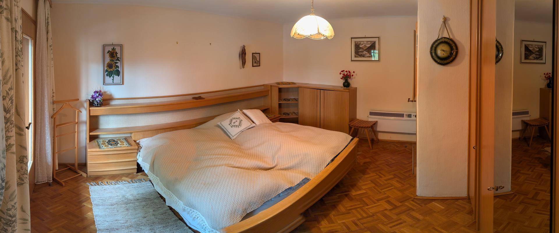 Helles Schlafzimmer mit Doppelbett, Holzboden und schlichten Holzmöbeln.