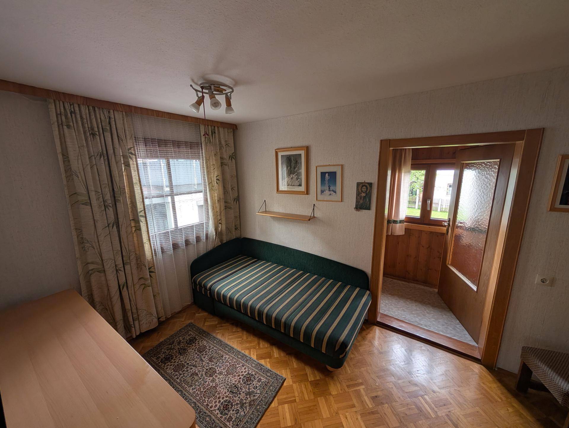 Kleines Schlafzimmer mit Einzelbett, Holzboden und Fenster mit Vorhängen.