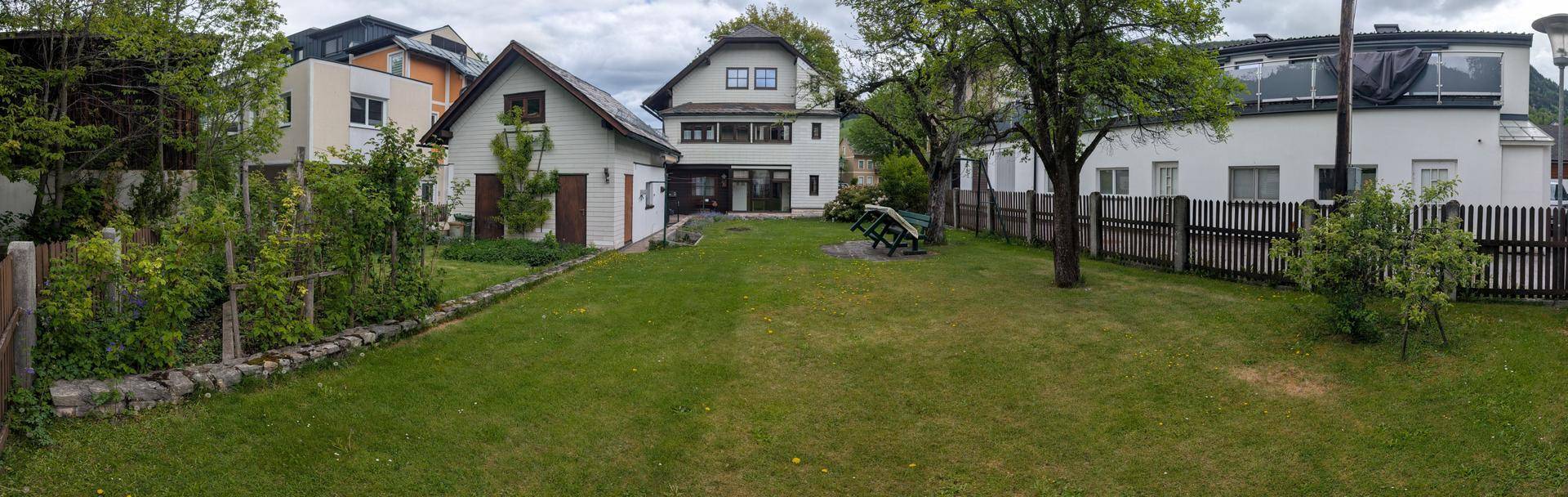 Weitläufiger Rasengarten mit Zaun und Bäumen, umgeben von mehreren Wohnhäusern.