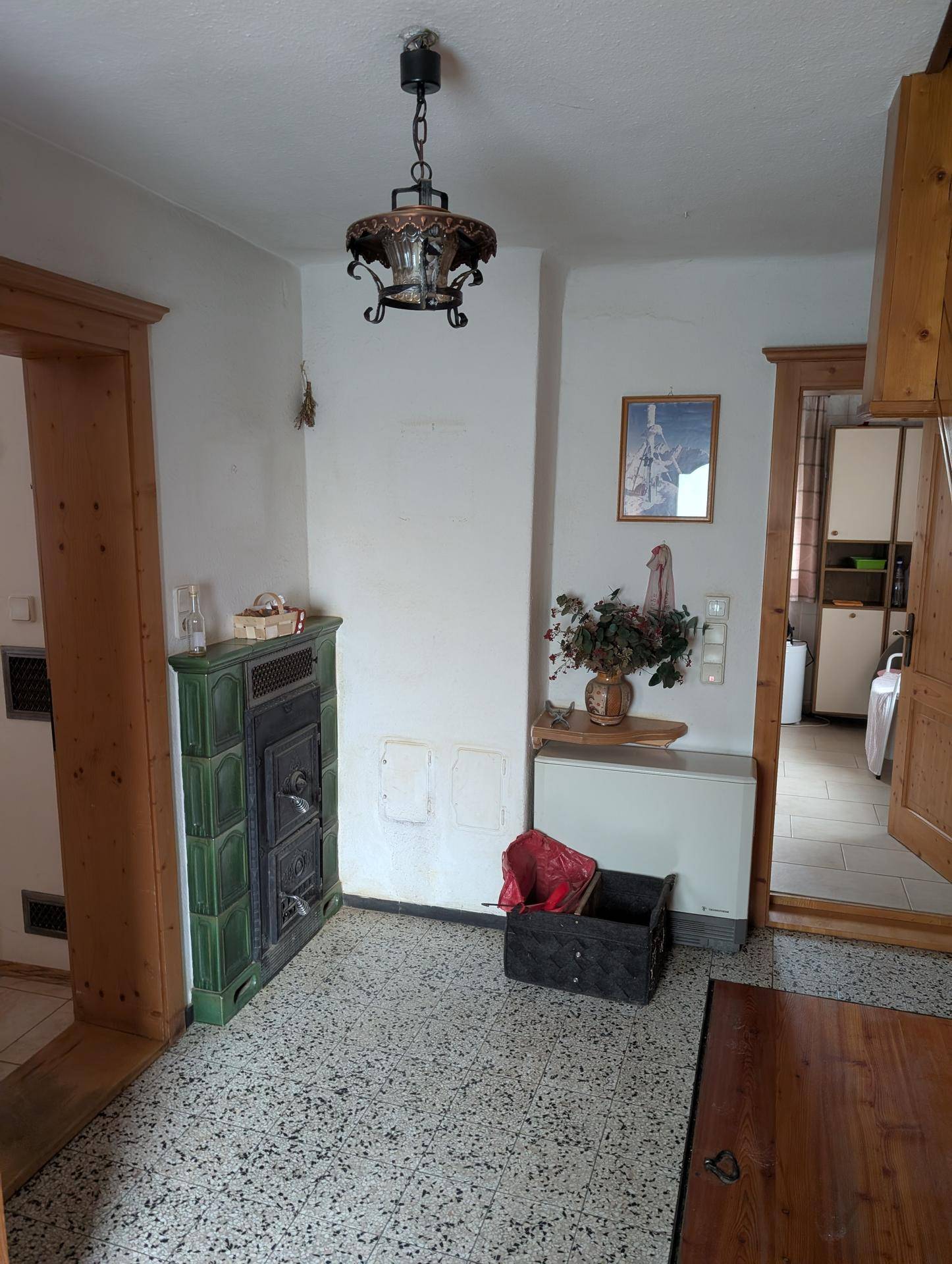Flur mit traditionellem Kachelofen, Terrazzoboden und Holztüren.