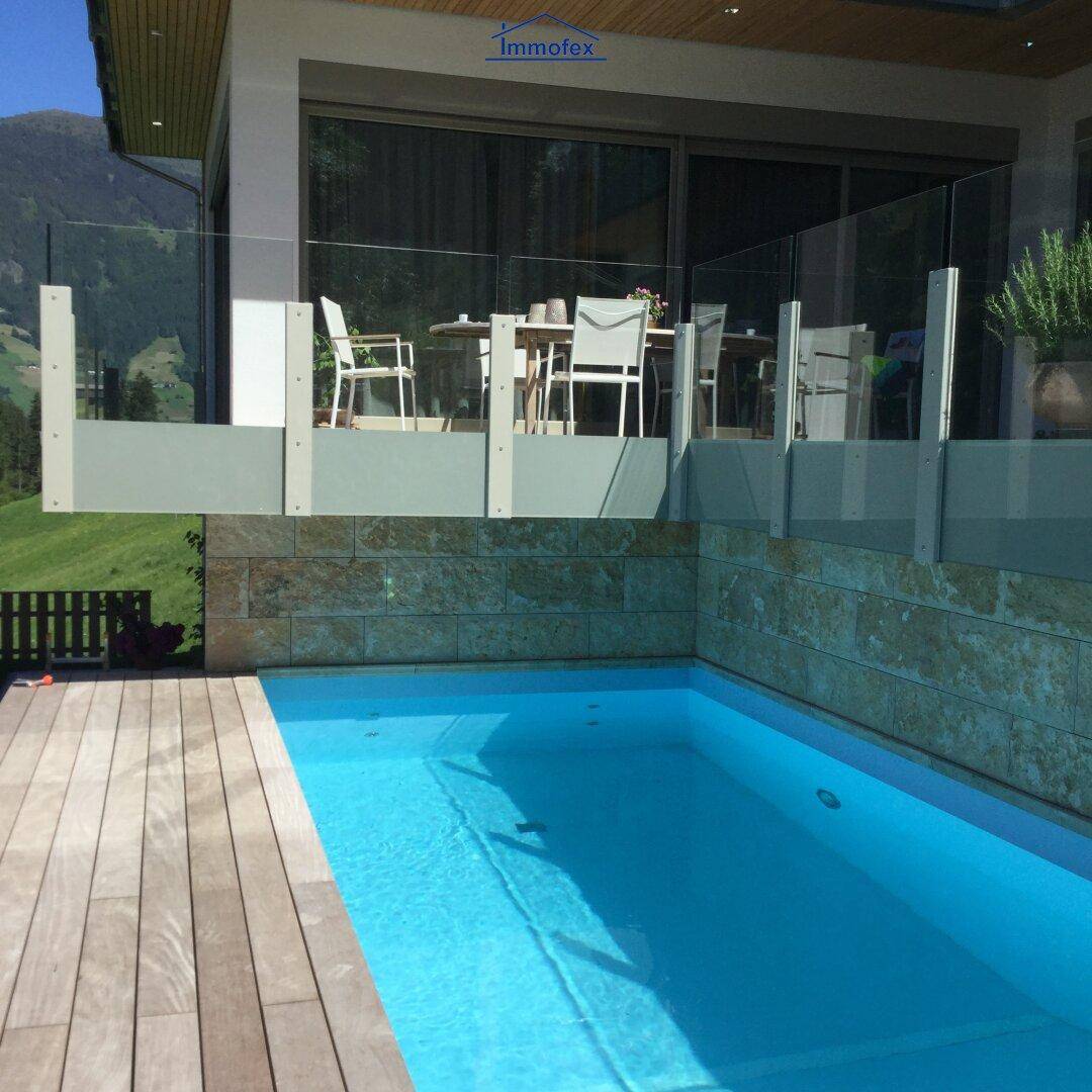 Außenpool mit Holzdeck und einer darüberliegenden Terrasse, umgeben von einer Steinmauer.
