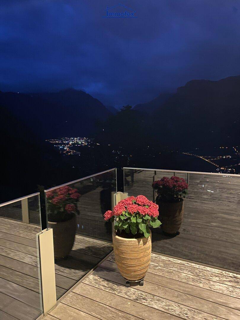 Terrasse bei Nacht mit beleuchteten Blumenkübeln und einem weiten Blick auf das beleuchtete Tal.