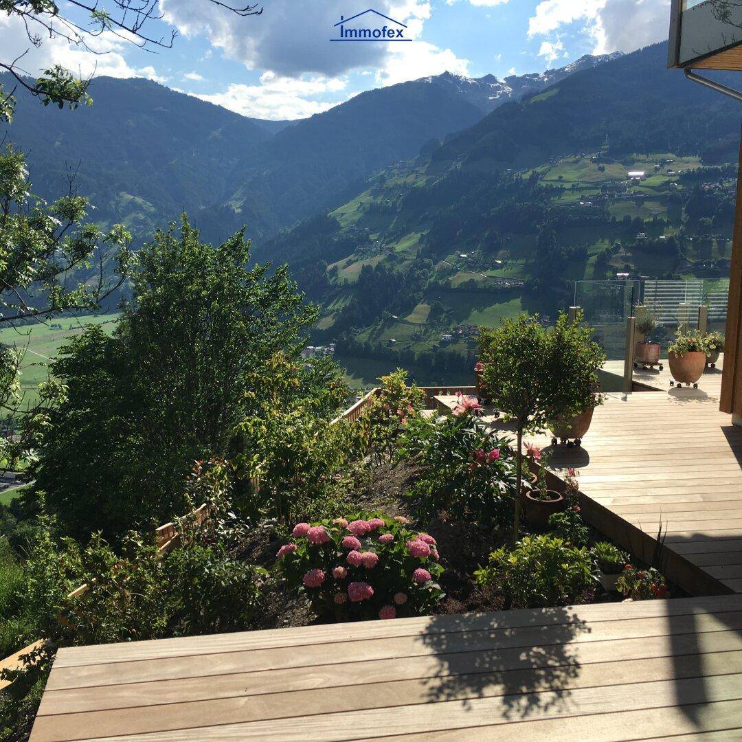 Gepflegter Gartenbereich mit blühenden Pflanzen und einer Holzterrasse, die einen weiten Bergblick bietet.