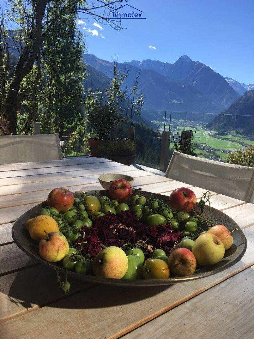 Terrasse mit Holztisch und einer Schale voller Früchte, umgeben von einer malerischen Bergkulisse.