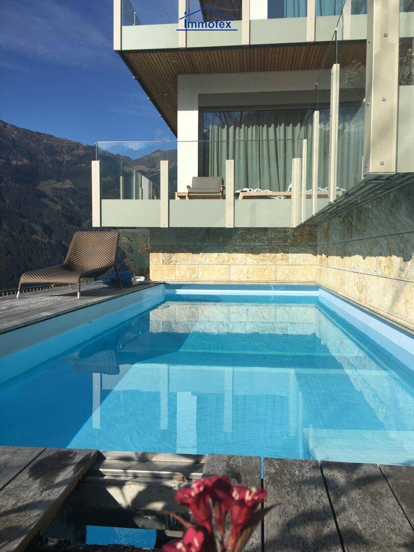 Moderner Außenpool mit Holzdeck und Blick auf die Architektur des Gebäudes und die Berge.