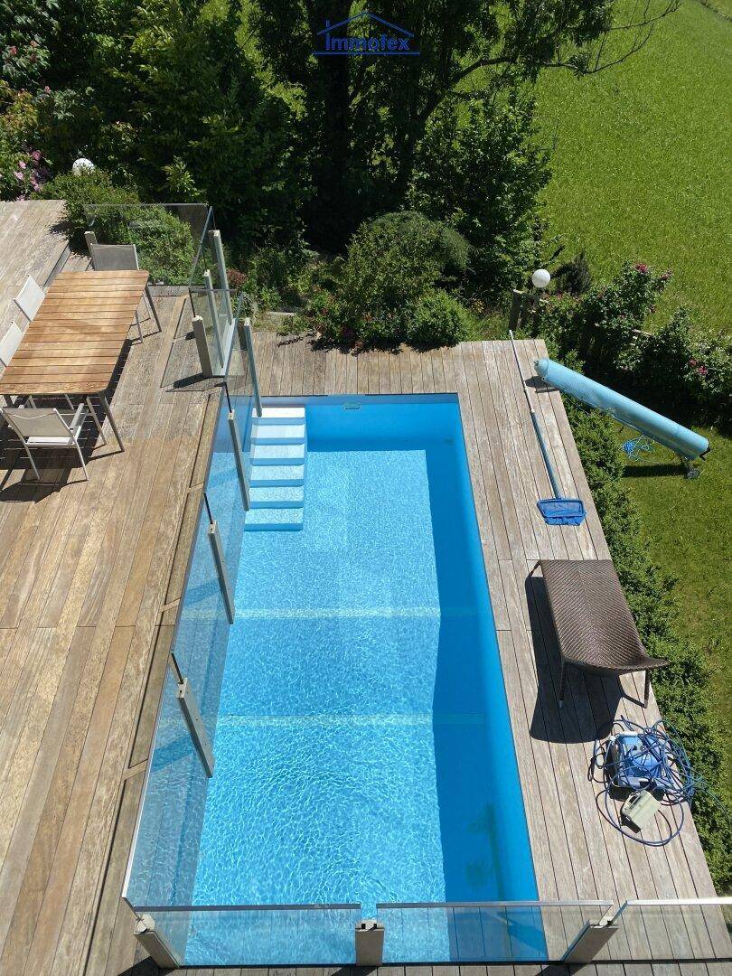 Vogelperspektive eines rechteckigen Pools mit Holzdeck, Liegefläche und Rutsche im Garten.