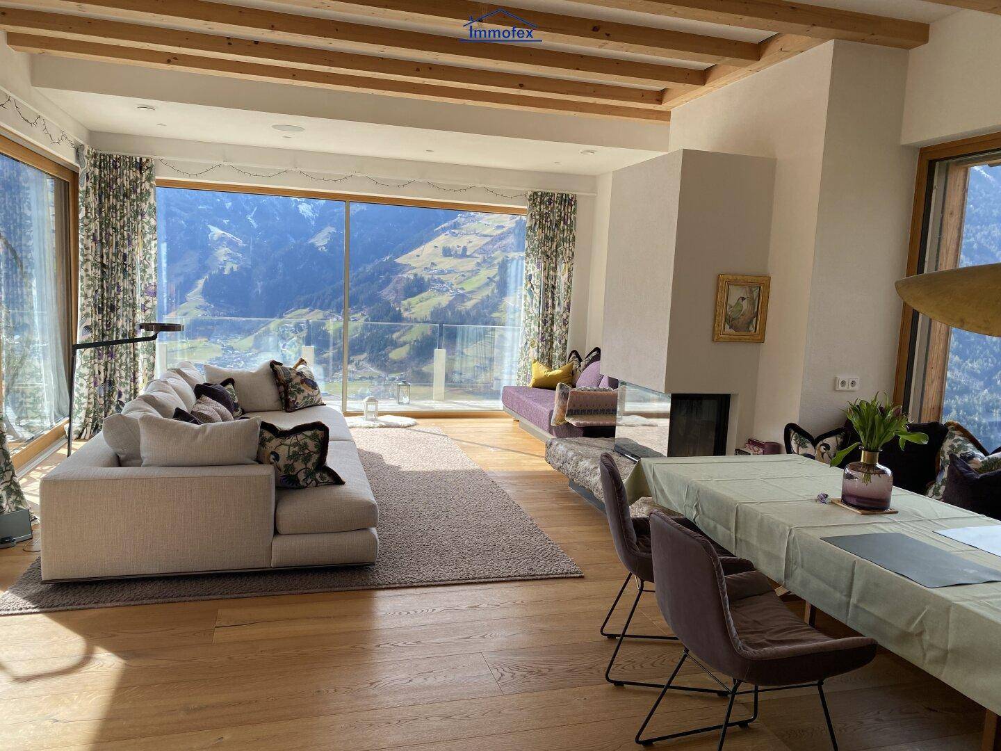 Großzügiger Wohn- und Essbereich mit Holzbalken, Kamin und Panoramablick auf die Bergwelt.