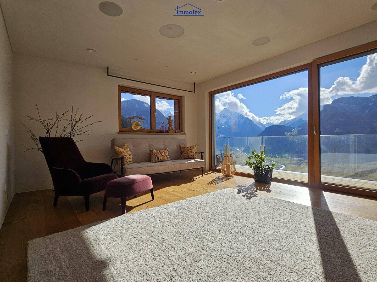 Helles Wohnzimmer mit Holzboden, gemütlichen Möbeln und großen Fenstern mit Bergblick.