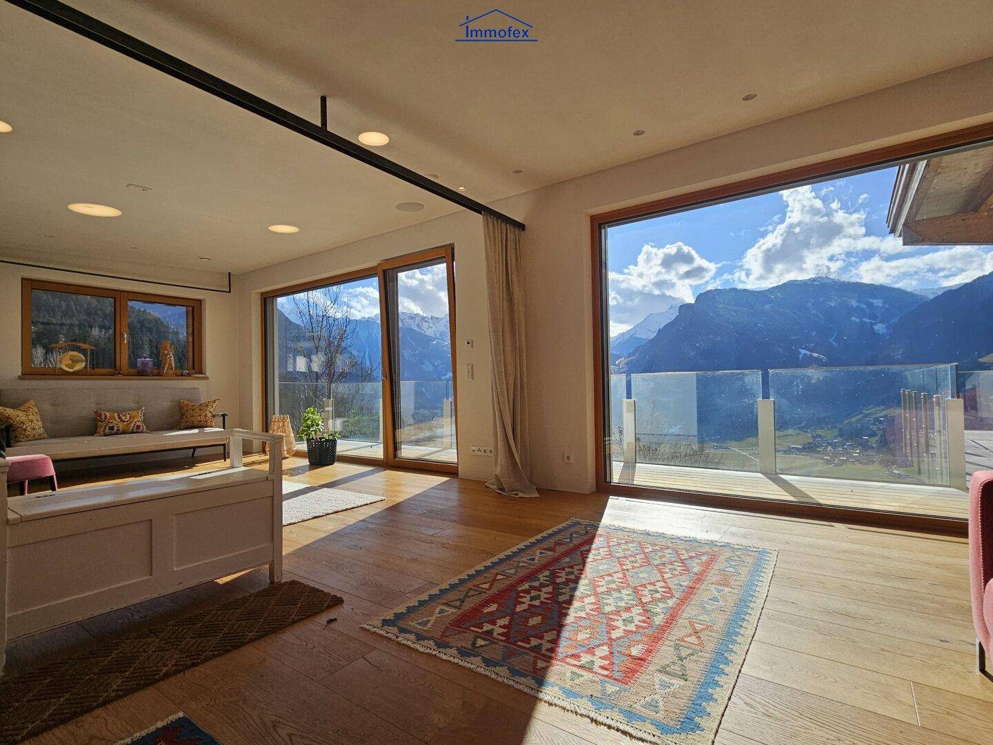 Lichtdurchfluteter Wohnbereich mit Holzboden, Teppich und Zugang zu einer Terrasse mit Bergblick.