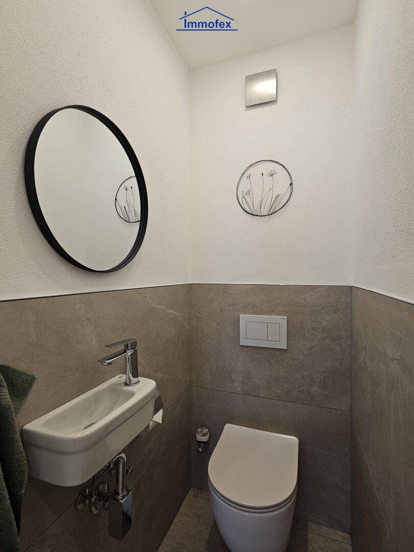 Modernes Gäste-WC mit Wand-WC und kleinem Waschbecken, elegant gefliest.