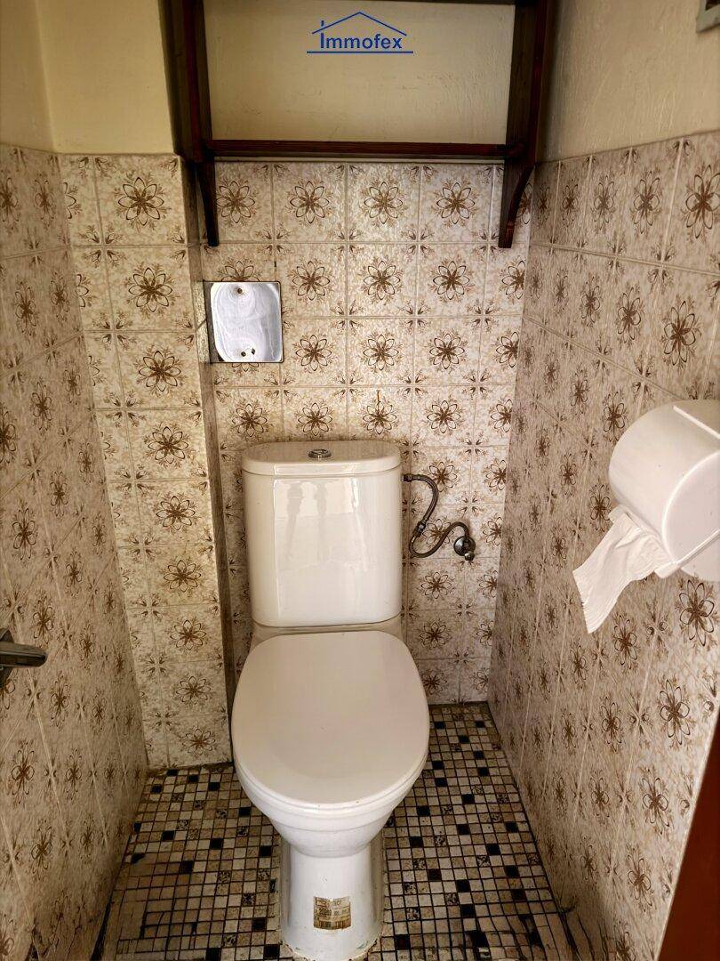 Separate Toilette mit gemusterten Fliesen und weißer Keramik, typisch für ältere Gebäude.