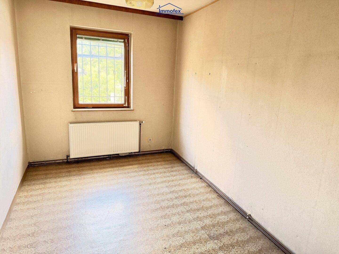 Kleines Zimmer mit gemustertem Laminatboden, Holzdecke und einem Fenster, das Tageslicht spendet.