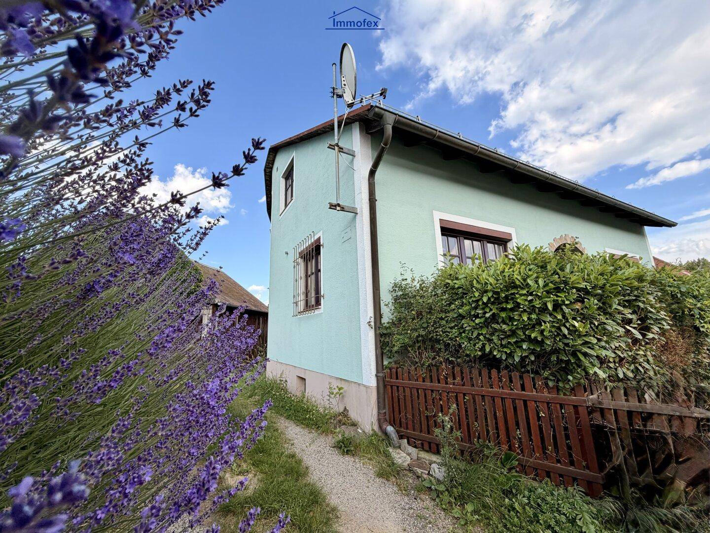 Seitenansicht des Hauses mit hellblauer Fassade, Holzzaun und blühendem Lavendel im Vordergrund.