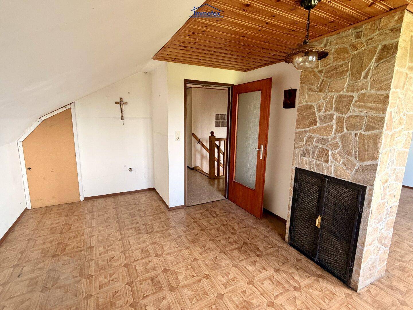 Dachgeschosszimmer mit Holzbalkendecke, Steinwandkamin und gemustertem Laminatboden.