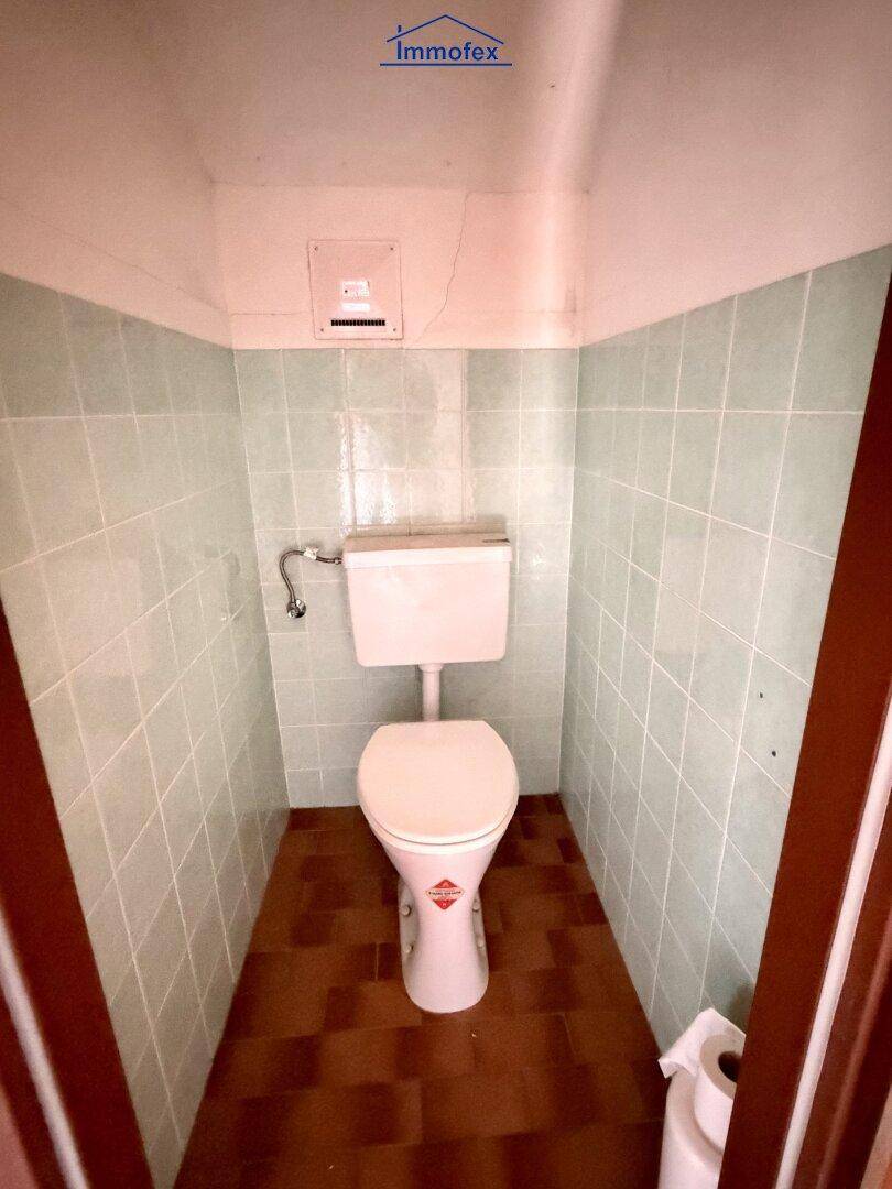 Kleine Toilette mit hellgrünen Fliesen und weißer Keramik, einfach und funktional.