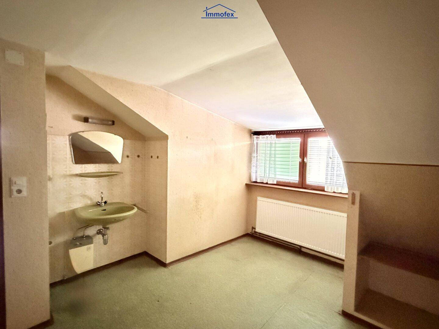 Dachgeschossraum mit Waschbecken, schrägen Wänden und Fenster, renovierungsbedürftig.