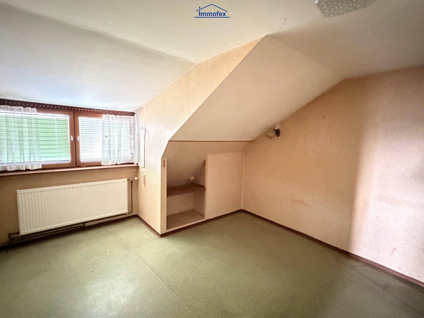 Dachgeschosszimmer mit schrägen Wänden, Fenster und integrierten Ablageflächen.