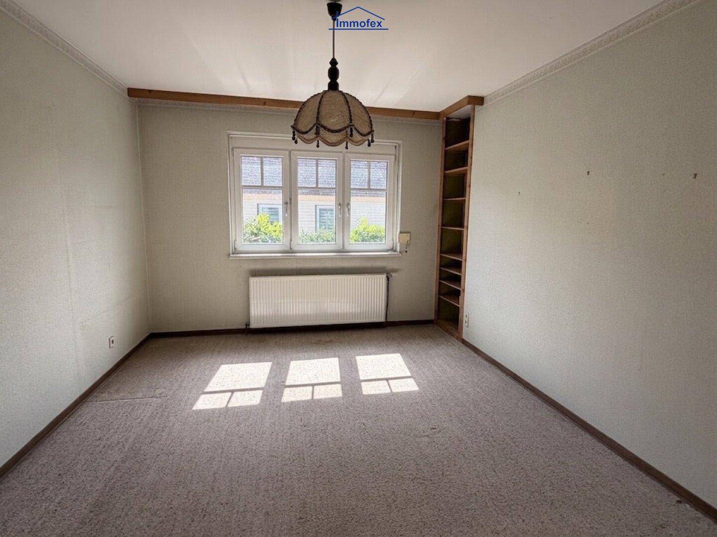 Helles Zimmer mit gemustertem Laminatboden, drei Fenstern und einem Einbauregal an der Wand.