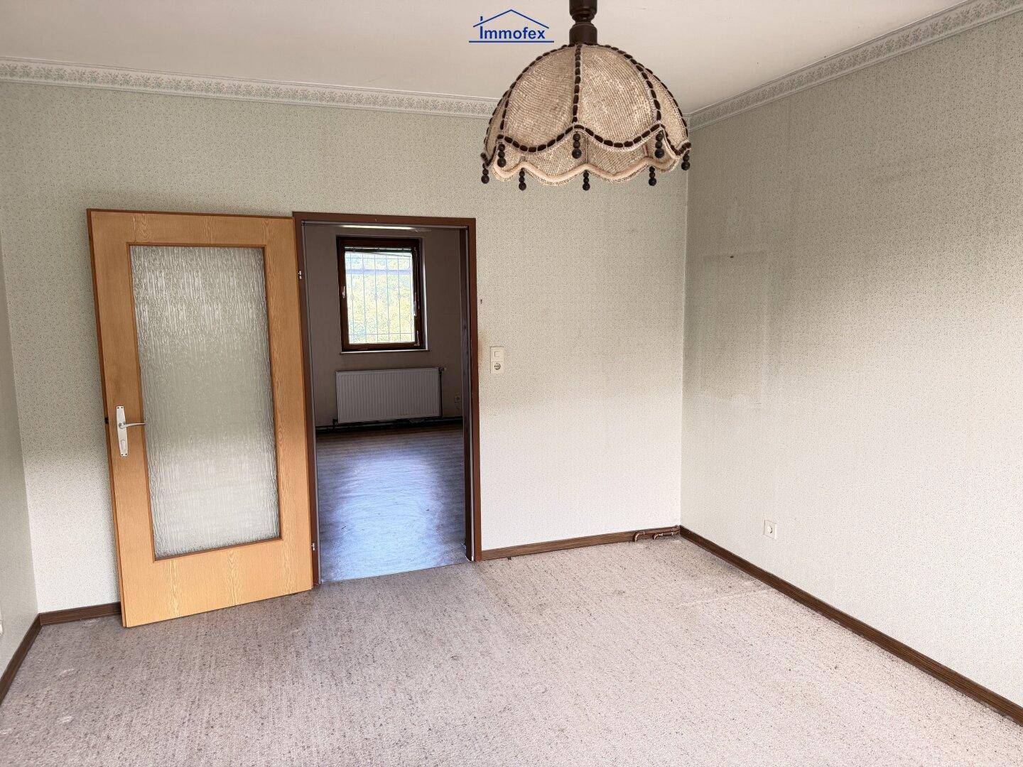 Leeres Zimmer mit gemustertem Laminatboden und einer Tür, die zu einem weiteren Raum führt.
