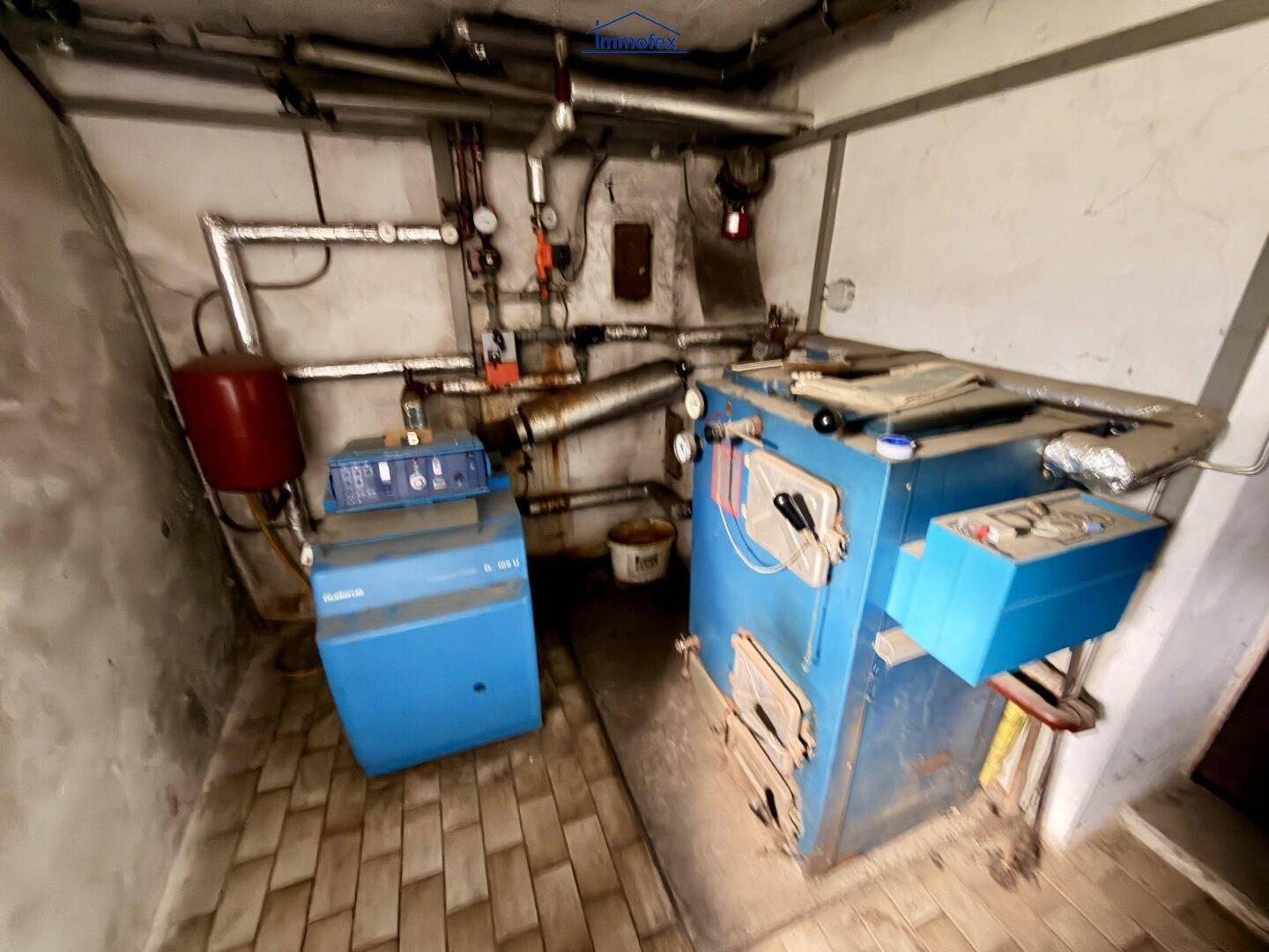 Heizungsraum im Keller mit zwei großen Heizkesseln und sichtbaren Rohren.