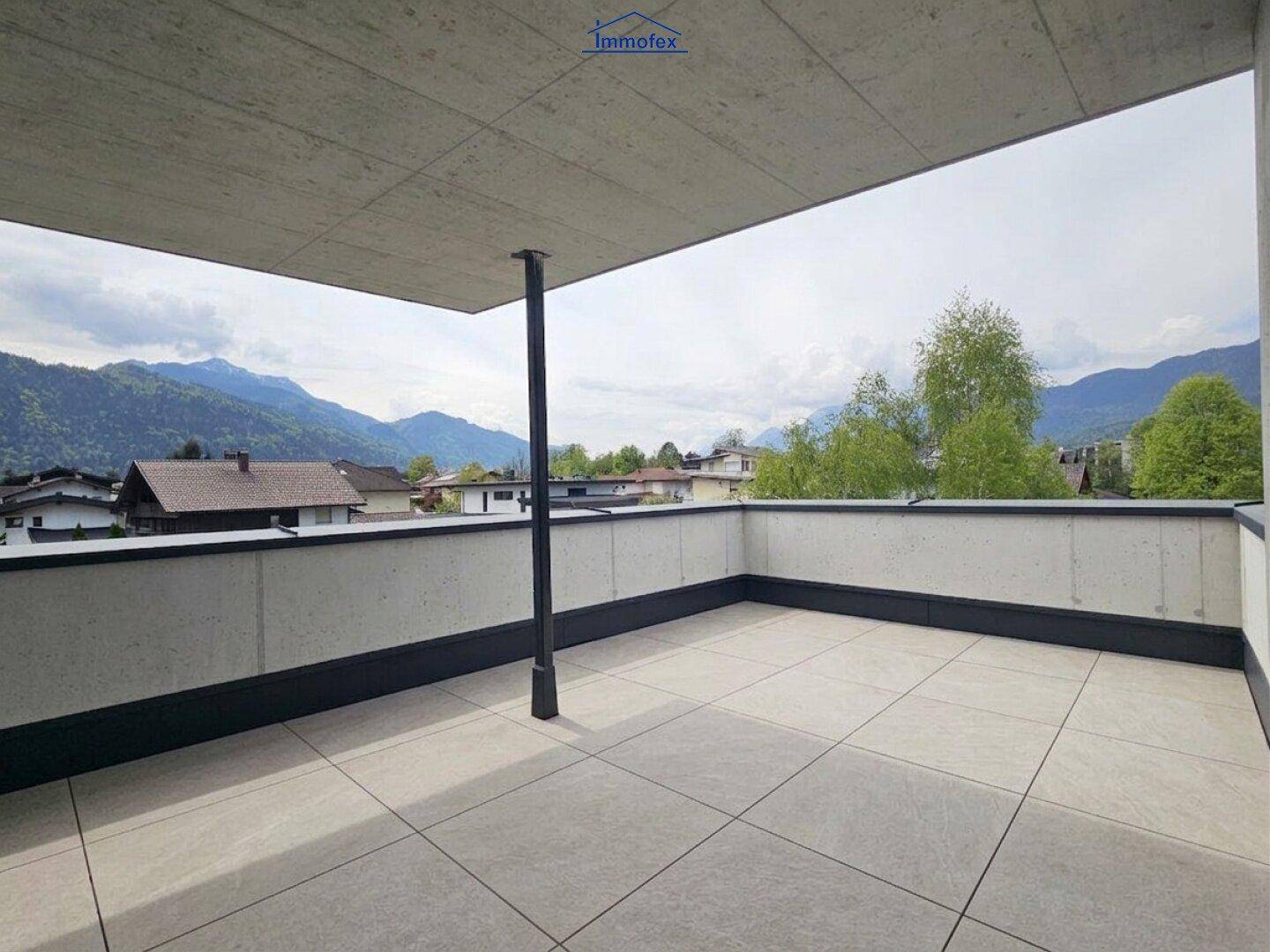 Geräumige Terrasse mit modernen Fliesen, Betonwänden und einem beeindruckenden Bergblick in die Ferne.