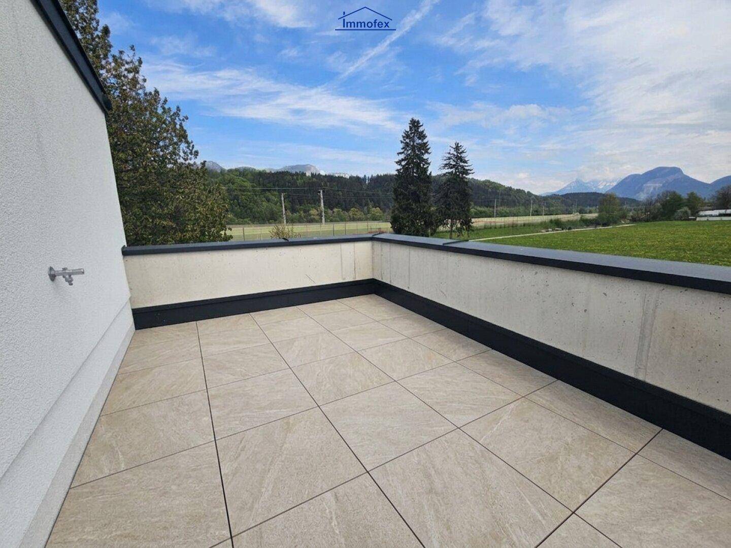 Sonniger Balkon mit beigen Fliesen und Panoramablick über Felder und die umliegende Berglandschaft.