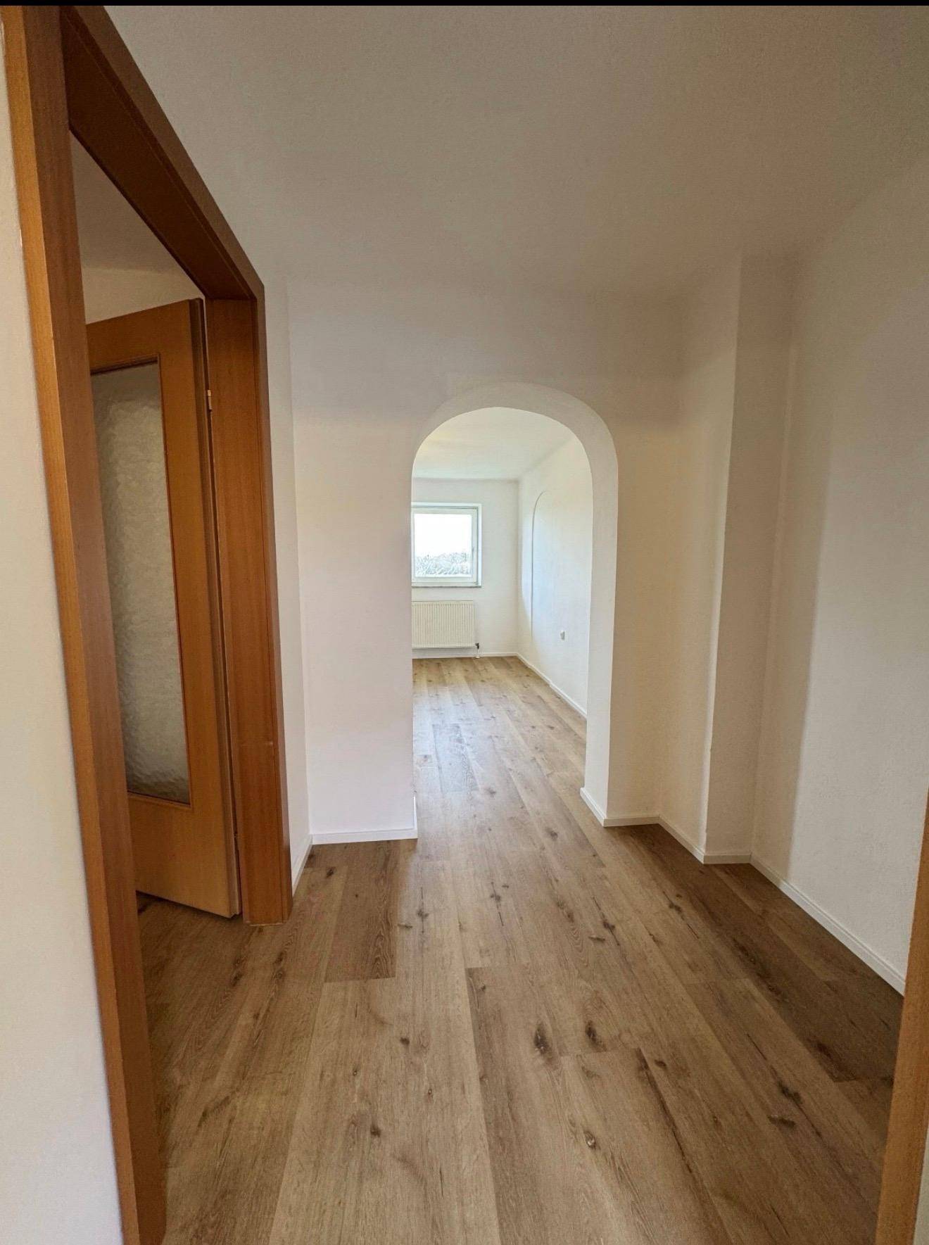 Langer Flur mit Holzboden, weißen Wänden und einem eleganten Rundbogen, der zu weiteren Räumen führt.