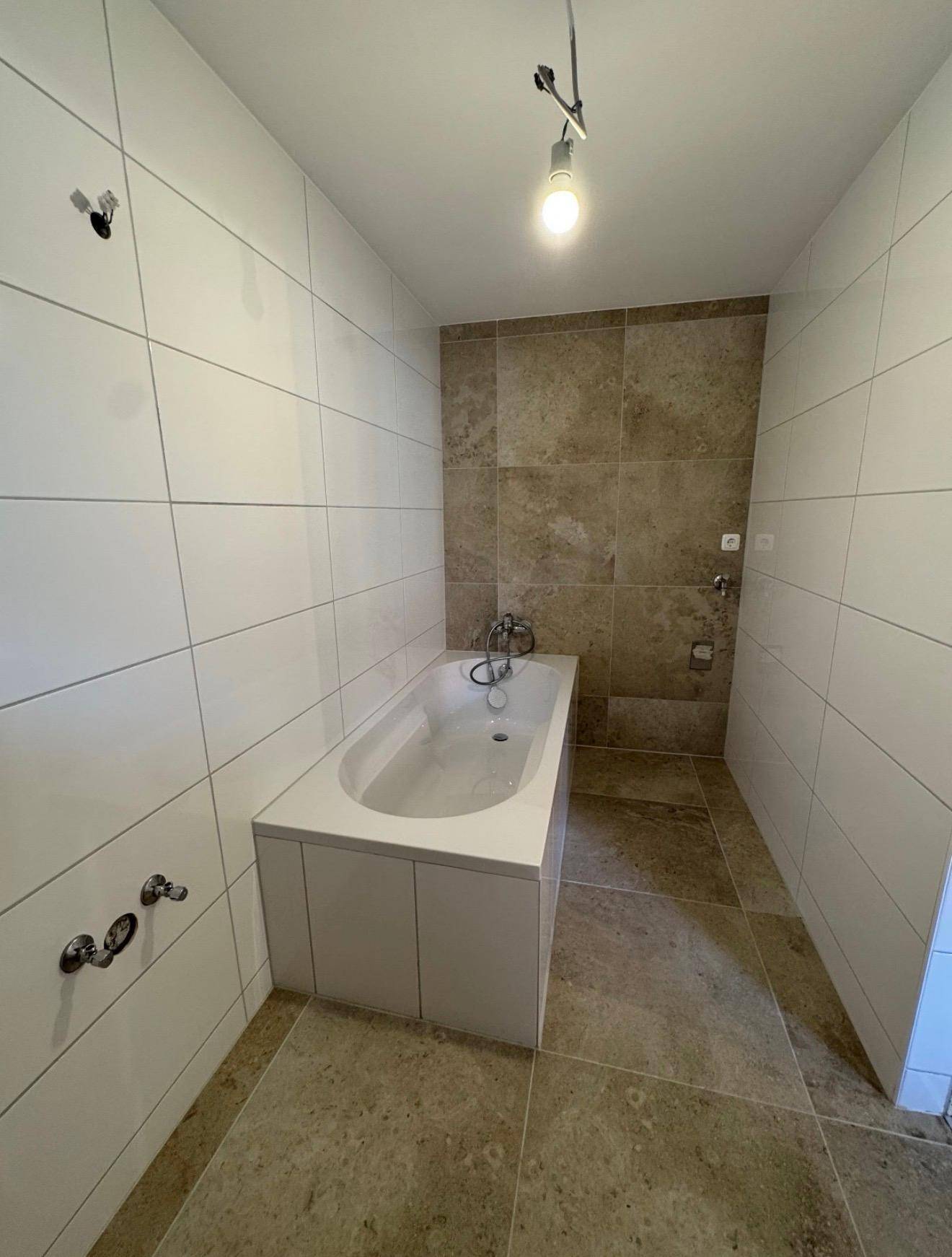 Badezimmer mit eingebauter Badewanne, weißen Wandfliesen und beigefarbenen Boden- und Akzentfliesen.