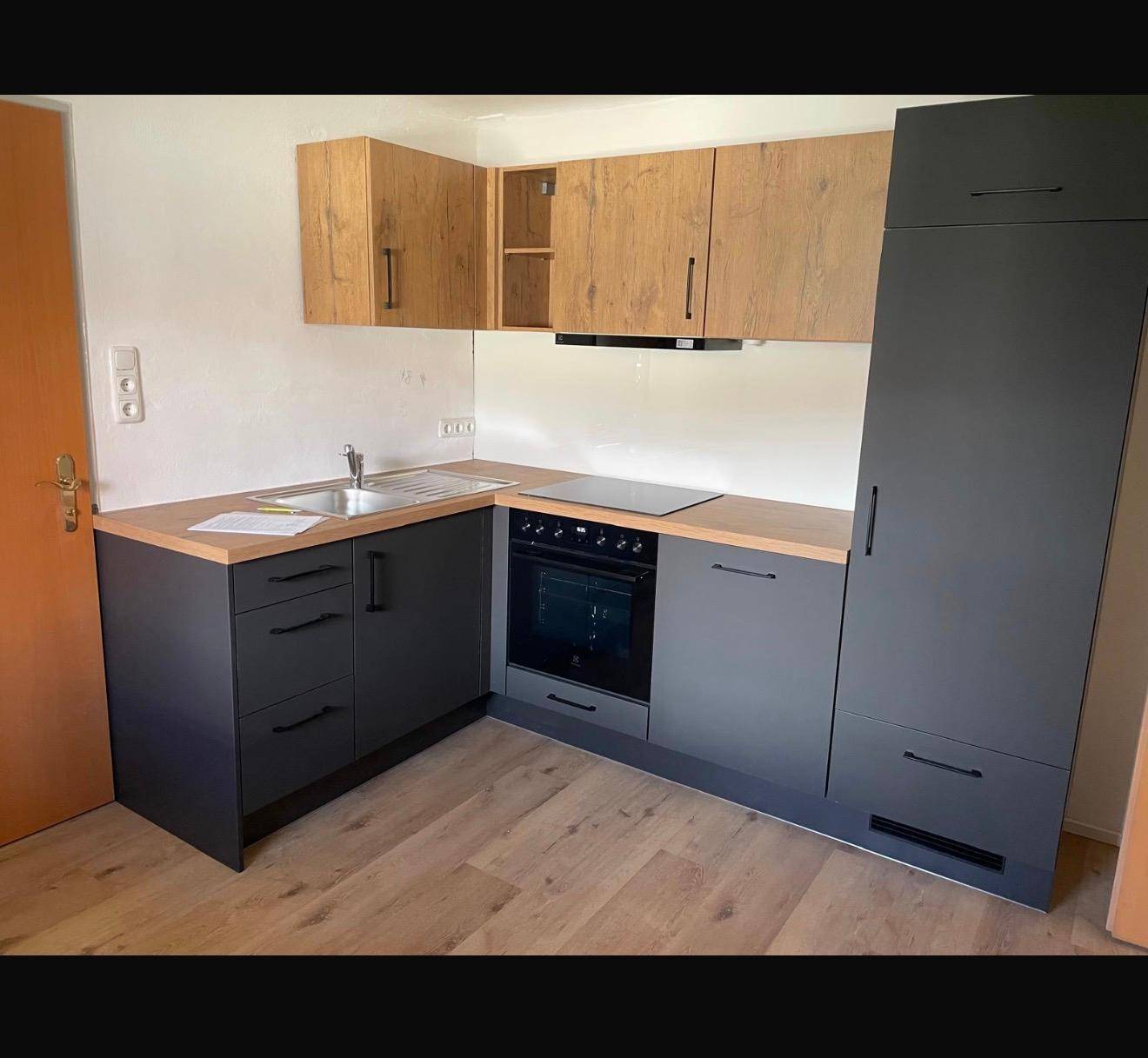 Moderne L-förmige Küche mit dunklen Unterschränken, Holz-Oberschränken und integrierten Geräten.