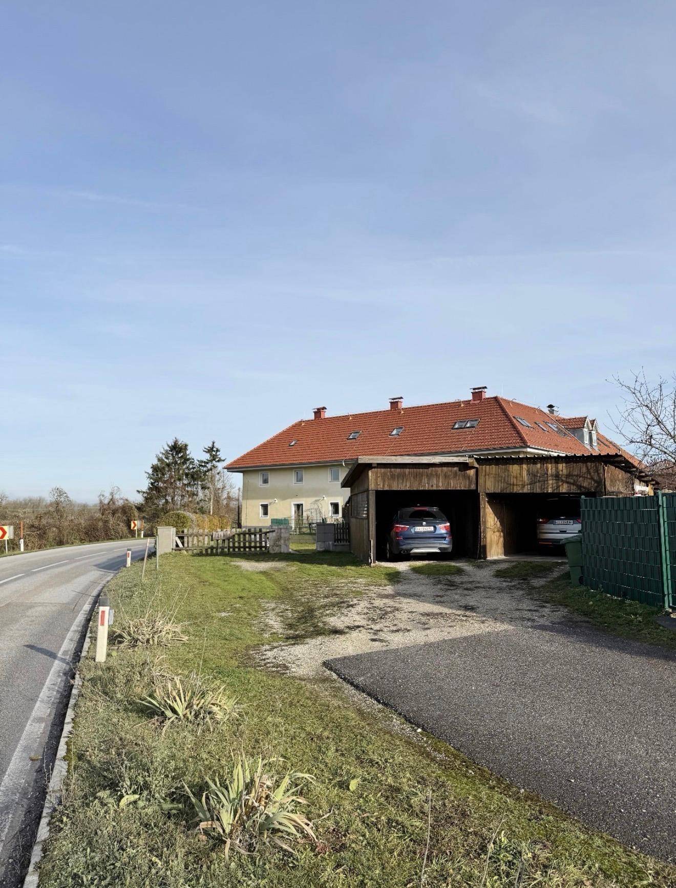 Landhaus mit rotem Ziegeldach, Holz-Carport für zwei Fahrzeuge und angrenzender Landstraße.